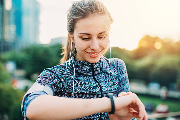 Sportswoman checking her smart watch Close-up of a young woman in sports wear and with portable information devices outdoors at urban setting pedometer stock pictures, royalty-free photos & images