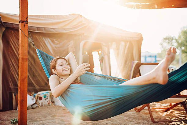 Texting in the hammock Smiling girl with smart phone resting in a hammock in a summer camp. girls laying on beach stock pictures, royalty-free photos & images