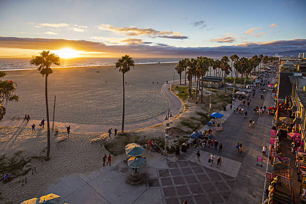 Tourists walking on footpath by beach during sunset High angle view of Venice beach during sunset. Tourists are walking on footpath by ocean. Shot of beautiful nature and people is taken from above. los angeles county stock pictures, royalty-free photos & images