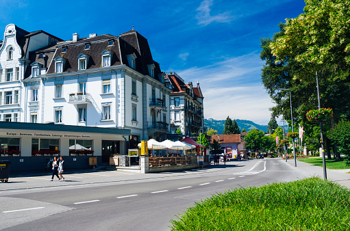 Interlaken, Switzerland - July 07, 2016: Tourists walking along the Hoheweg, near the turnoff for the Beaurivage Bridge, in the alpine resort of Interlaken in the Bernese Oberland region of Switzerland on a sunny summers day. On the left is Johnny's Pub and grill, restaurant Shalimar and the Hotel Carlton Europe.