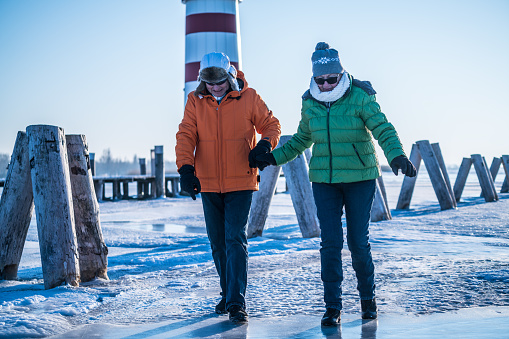 senior couple walking cautious on deep frozen lake neusiedl in austria wearing warm clothes winter blue sky sunny day light house