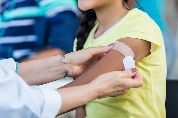 Doctor applies bandage to preteen girl's arm following an immunization Unrecognizable female doctor applies an adhesive bandage to preteen girl's arm after the girl receives a flu shot at an outdoor free clinic. flu vaccine photos stock pictures, royalty-free photos & images