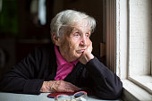 An elderly woman sadly looking out the window.