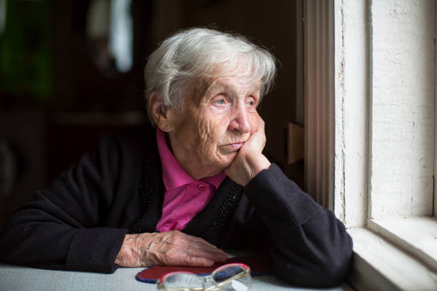 an elderly woman sadly looking out the window. - abandonado imagens e fotografias de stock