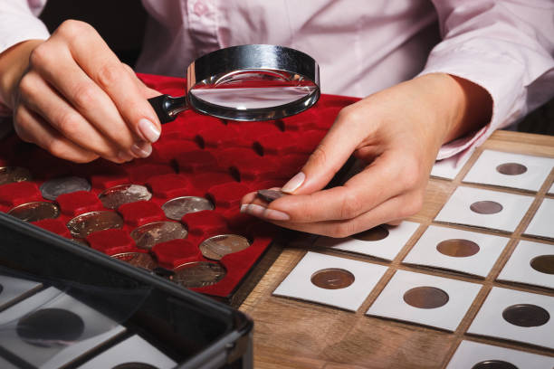 Woman looks at the coin through a magnifying glass Woman looks at the coin through a magnifying glass, soft focus background coin collection stock pictures, royalty-free photos & images
