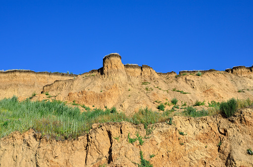 Deep sandy cliff on the background of blue sky. The destruction of the coast as a consequence of soil erosion.