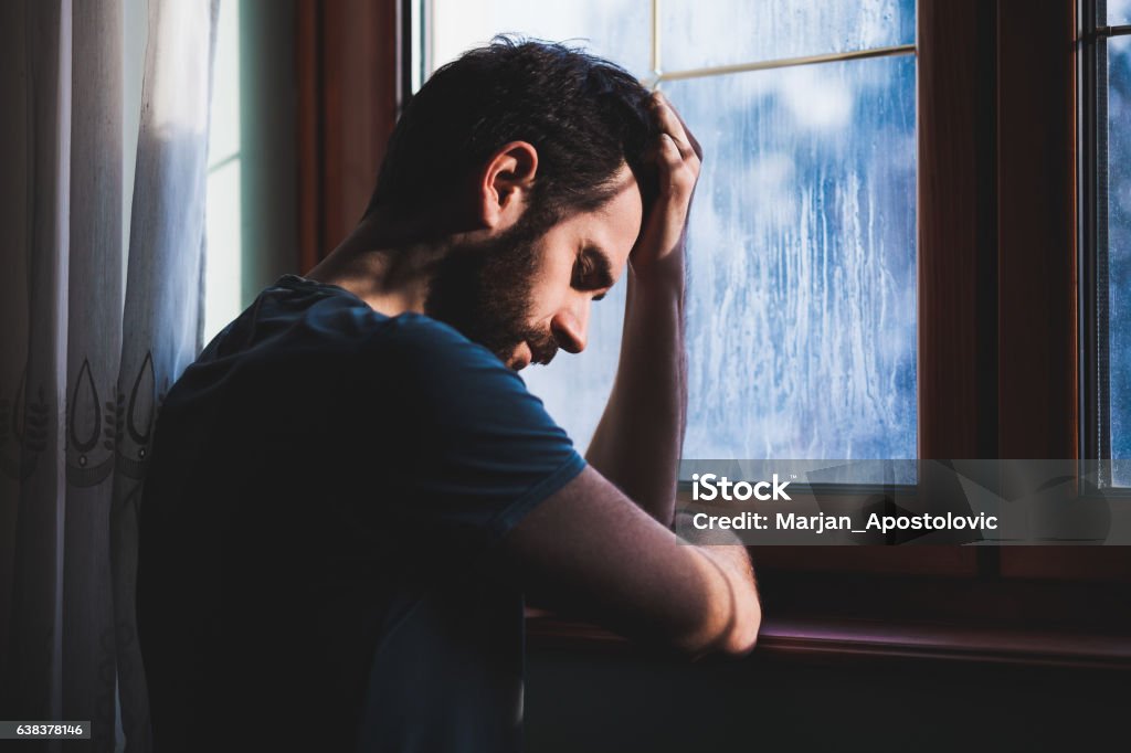Young sad mad sitting in regret Young sad mad sitting by the window in regret Men Stock Photo