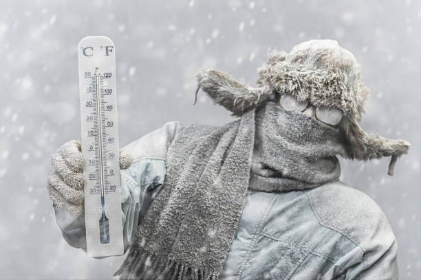 Frozen man holding a thermometer while it is snowing stock photo