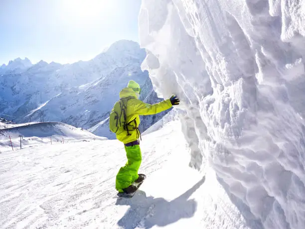 Snowboarder riding along ice wall in ski resort at mountain background