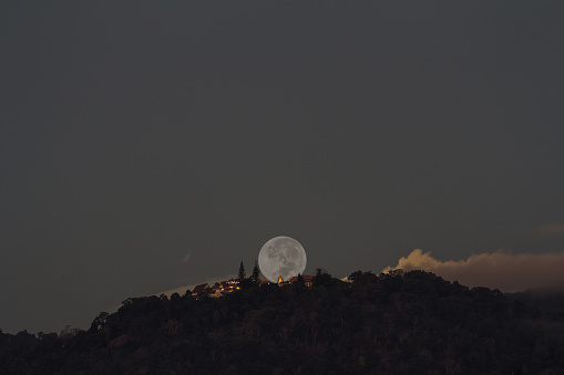 Supermoon setting over Buddhist temple on mountain at early morning, focus at temple