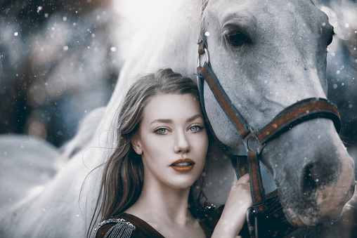 fashion model portrait in winter day posing side by side with white horse.looking at camera, friendship concept.