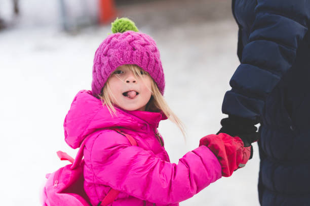 winter close up portrait of adorable blond girl in preschool age holding her parent for hand and walking outdoors