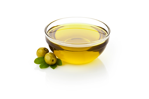Olive oil and green olives with leaves in glass bowl sitting on reflective white backdrop.  DSRL studio photo taken with Canon EOS 5D Mk II and Canon EF 70-200mm f/2.8L IS II USM Telephoto Zoom Lens