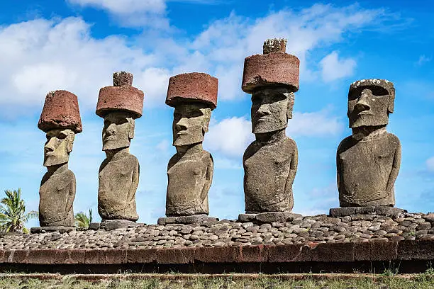 Moai side by side in a row with headgear at Anakena Beach under sunny summer sky. Anakena Beach, Rapa Nui National Park, Hanga Roa, Easter Island, Chile.