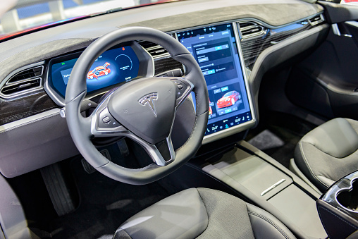 Brussels, Belgium - January 13, 2017: Luxurious interior on a Tesla Model S full electric luxury car with a large touch screen and dashboard screen. The car is fitted with leather seats and aluminium details. The Model S is one of the world's top selling plug-in electric cars and this 75D is fitted with All Wheel Drive and autopilot. The car is displayed on a motor show stand, with lights reflecting off of the body.