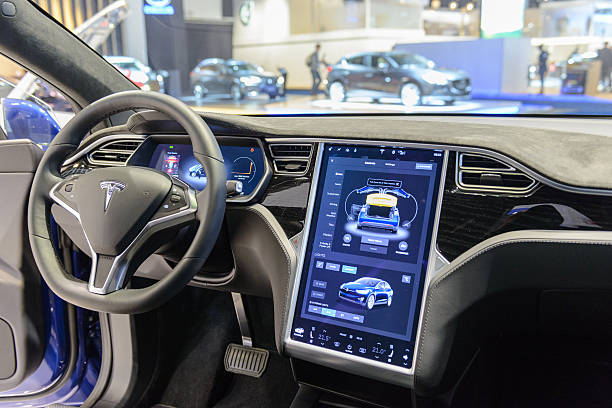 Tesla Model X 90D electric luxury high tech interior Brussels, Belgium - January 13, 2017: Luxurious interior on a Tesla Model X 90D full electric luxury crossover SUV car with a large touch screen and dashboard screen. The car is fitted with leather seats and aluminium details. The Model X uses falcon wing doors for access to the second and third row seats. The car is displayed on a motor show stand, with lights reflecting off of the body. There are people looking around and other cars on display in the background. empty dealership interior stock pictures, royalty-free photos & images