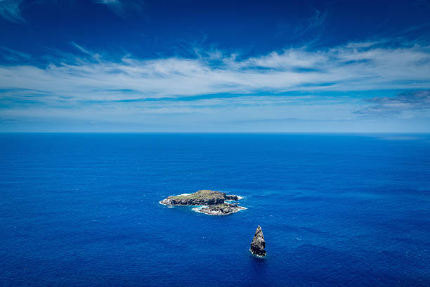 An old, historic red sculpture, made of red volcanic rock, stands on a beige pedestal on the coast of Easter Island above the Pacific Ocean