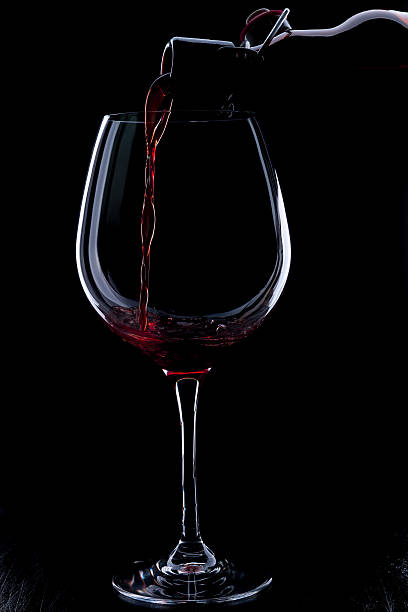 istock Red wine pouring into a wineglass. Isolated on black background. 638439318
