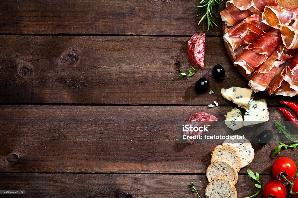 Appetizer border on rustic wood table Top view of a rustic wood table with delicatessen like prosciutto, salami, black olives, crostini, blue cheese and some herbs at the right border leaving a useful copy space.  DSRL studio photo taken with Canon EOS 5D Mk II and Canon EF 100mm f/2.8L Macro IS USM Meat Stock Photo