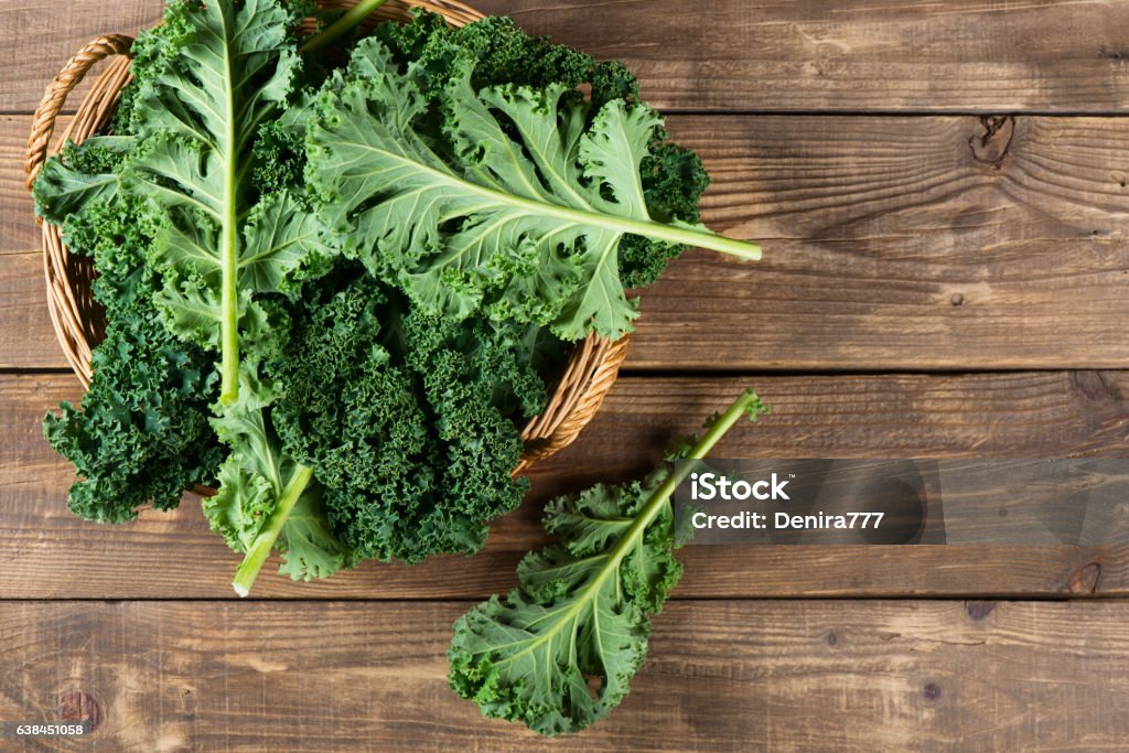 Leaves of  raw kale, above view. Top view of freshly harvested kale in a wicker basket on a rustic wooden background with copy space. Kale Stock Photo