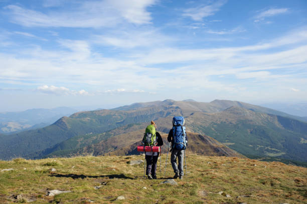Young couple walking together on the mountain summit enjoying beautiful open panoramic view and their hike together. Hiking equipment. Man and woman using trekking sticks.
