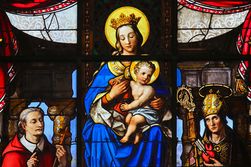 Ghent, Belgium - December 23, 2016: Stained Glass (1851) in Saint Nicholas Church, Ghent, depicting Mother Mary and the Infant Jesus, Madonna and Child, and the donors and various saints.