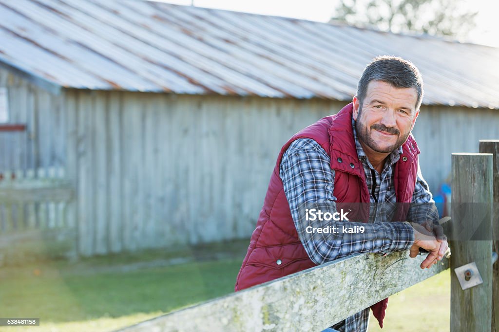 Homem do lado de fora do celeiro encostado em cerca de madeira - Foto de stock de Cena Rural royalty-free