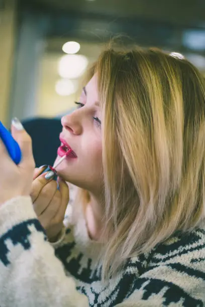 Photo of cute young girl putting red lipstick on lips