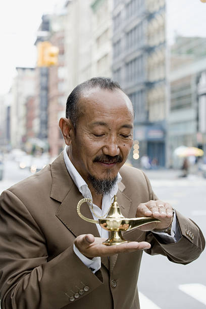 uomo maturo asiatico che sfrega la lampada del genio nel centro della città - sayings business aspirations magic foto e immagini stock