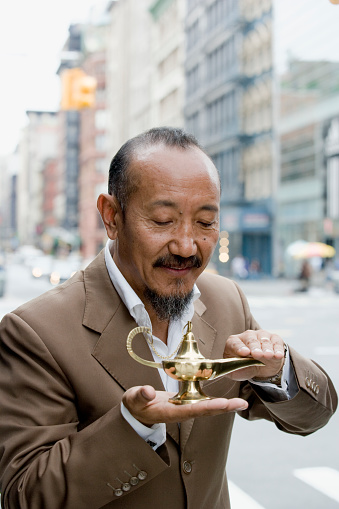 Asian mature man rubbing genie lamp in downtown city, New York City