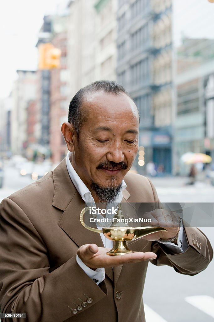 Asian mature man rubbing genie lamp in downtown city Asian mature man rubbing genie lamp in downtown city, New York City Magic Lamp Stock Photo