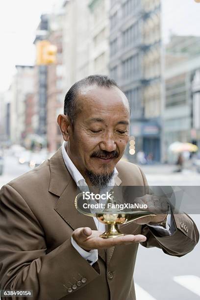 Asian Mature Man Rubbing Genie Lamp In Downtown City Stock Photo - Download Image Now