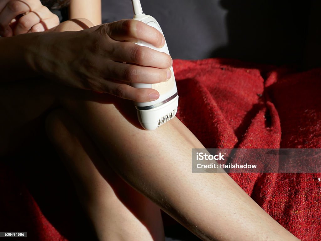 Woman epilating legs Removing hair with mechanical epilator. Adult Stock Photo