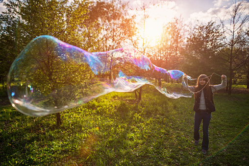 Little girl aged 10 having fun with big bubbles on spring evening. The smiling girl is holding a big bubble wand and making a huge bubbles. 