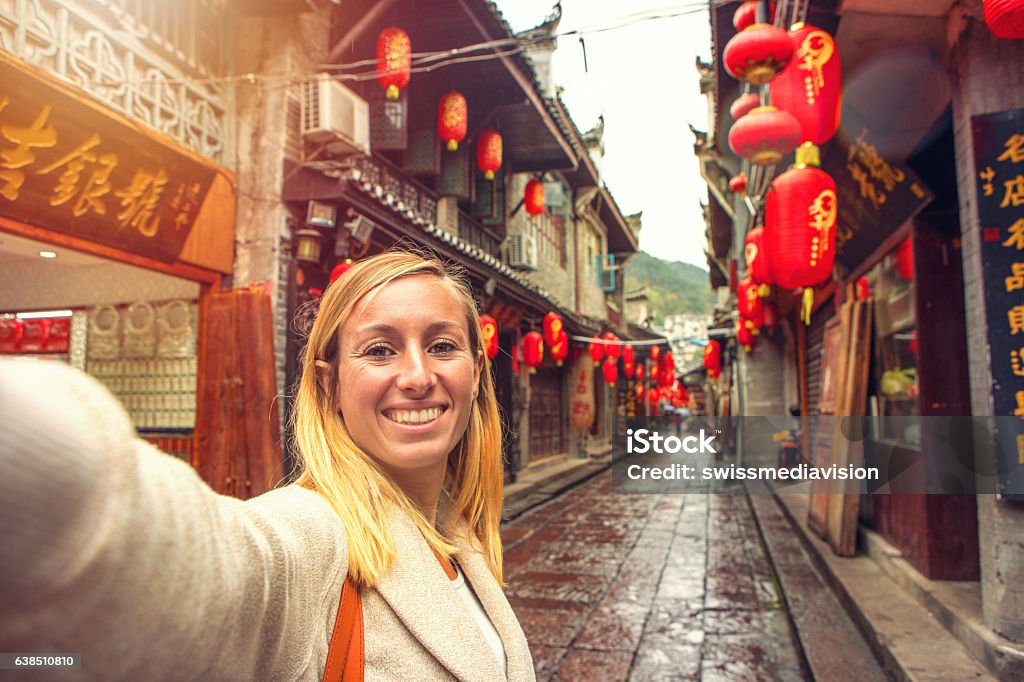 Young woman in Chinese street taking selfie portrait Young woman in an alley of the ancient village of fenghuang, China taking a selfie portrait. China - East Asia Stock Photo