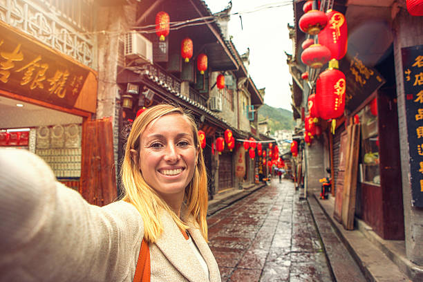 Young woman in Chinese street taking selfie portrait Young woman in an alley of the ancient village of fenghuang, China taking a selfie portrait. hunan province photos stock pictures, royalty-free photos & images