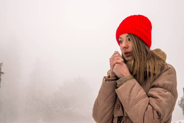 beautiful girl freezing in winter park. cold winter. portrait girl in a red cap and jacket warms her hands. Closeup portrait of beautiful young girl in winter day
