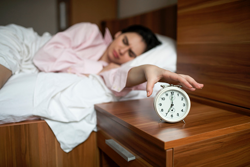 Young woman is awakening and turning off retro alarm clock