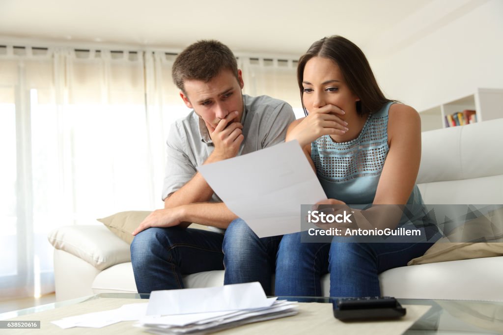 Worried couple reading a letter at home Worried couple reading a letter sitting on a couch in the living room at home Couple - Relationship Stock Photo