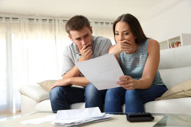 Worried couple reading a letter at home Worried couple reading a letter sitting on a couch in the living room at home sad disbelief stock pictures, royalty-free photos & images