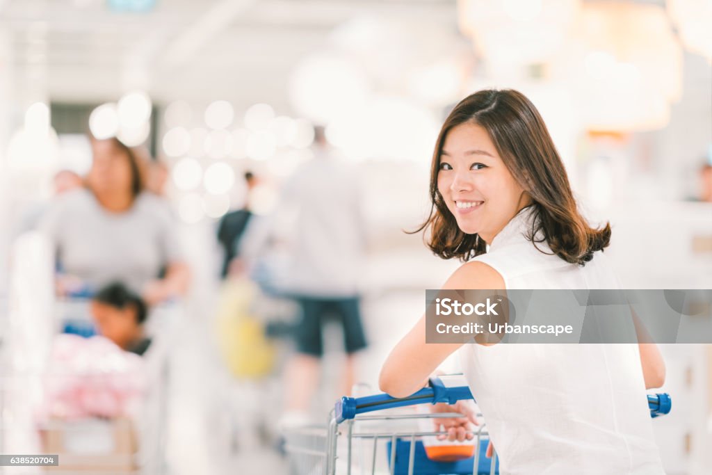 Asian woman with shopping cart at shopping mall Smiling Asian woman with shopping cart or trolley at department store or shopping mall, happy lifestyle or shopaholic concept, blur bokeh background with crowd and copy space Supermarket Stock Photo