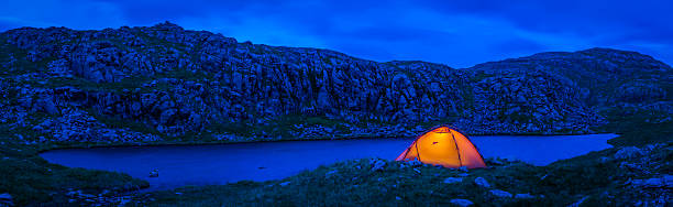 istock Warmly illuminated dome tent camping beside blue mountain lake panorama 638520820