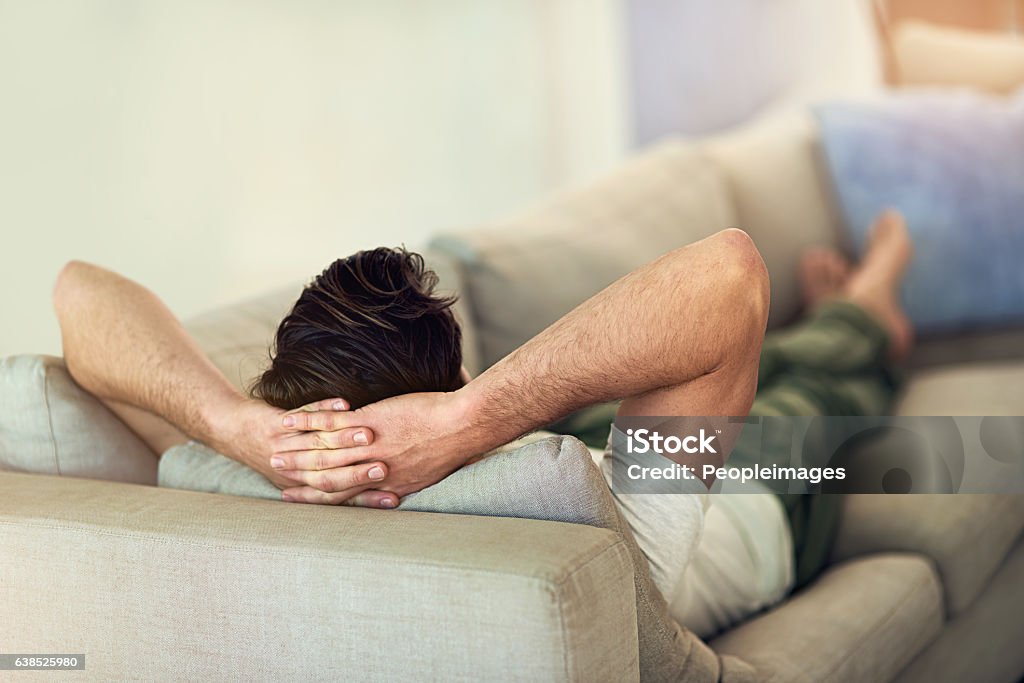 Feet up, wind down rearview shot of a young man relaxing on the sofa at home Men Stock Photo