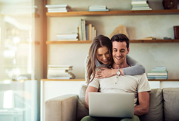 Show love everyday, in the simplest of ways Shot of a young woman hugging her husband while he uses a laptop on the sofa at home two people embracing stock pictures, royalty-free photos & images