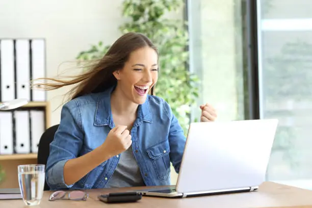 Excited entrepreneur working on line with a laptop at office and the hair moved by the wind