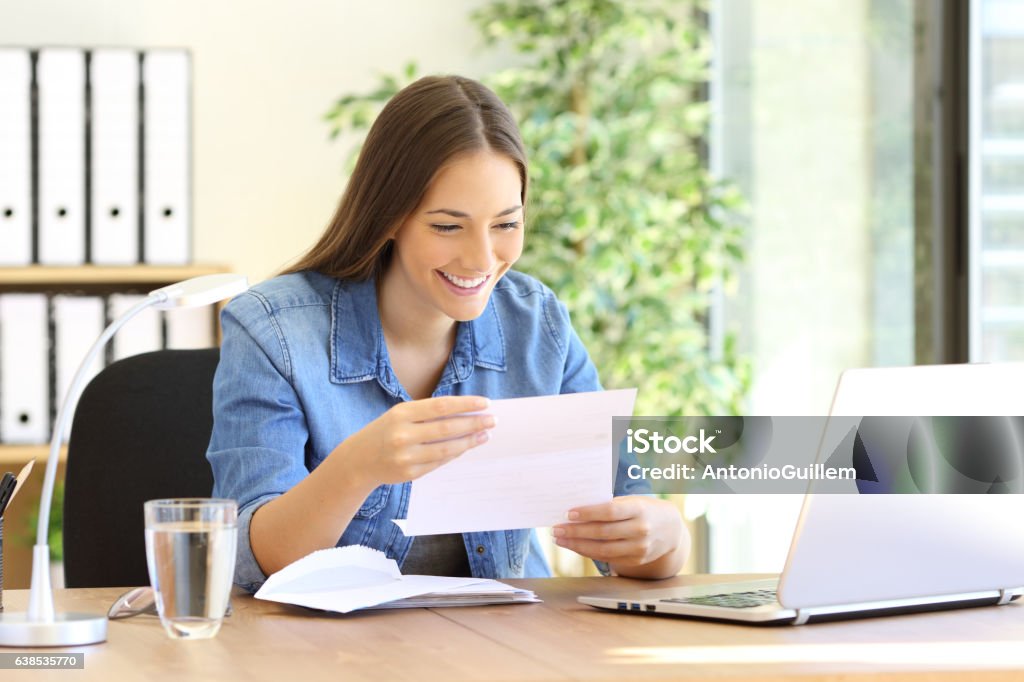 Entrepreneur woman reading a letter at office Happy entrepreneur woman reading good news in a letter in a desk at office Opening Stock Photo