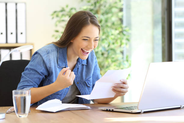 Excited entrepreneur girl reading a letter Excited casual entrepreneur girl reading good news in a letter in a desktop at office personal loan stock pictures, royalty-free photos & images