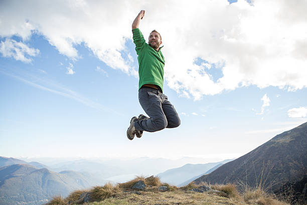 Young hiking man at the top of a mountain jumping high up for success. Swiss Alps and lake on the background. Autumn season.