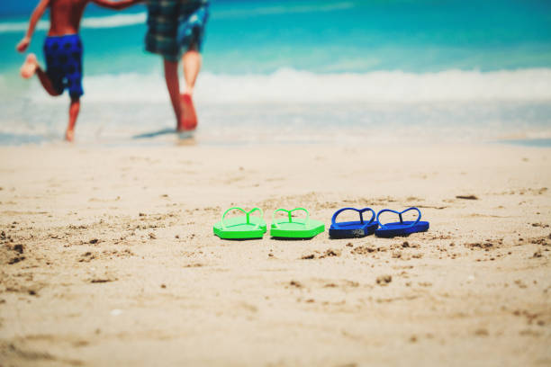 father and son go swim at beach, flip flops on sand