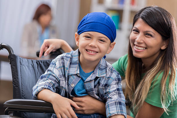 Young male cancer patient waits in waiting room Mid adult mom and her elementary age son wait in waiting room in doctor's office or hospital. The boy is wearing a blue cap and is sitting in a wheelchair. cancer illness stock pictures, royalty-free photos & images